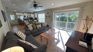 A living room with a sofa, a coffee table, and a balcony with a view of greenery.