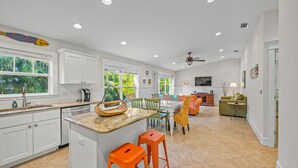 A spacious kitchen with white cabinets, a central island with stools, and a dining area with chairs and a table.