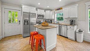 A modern kitchen with white cabinetry, stainless steel appliances, and a central island with stools.