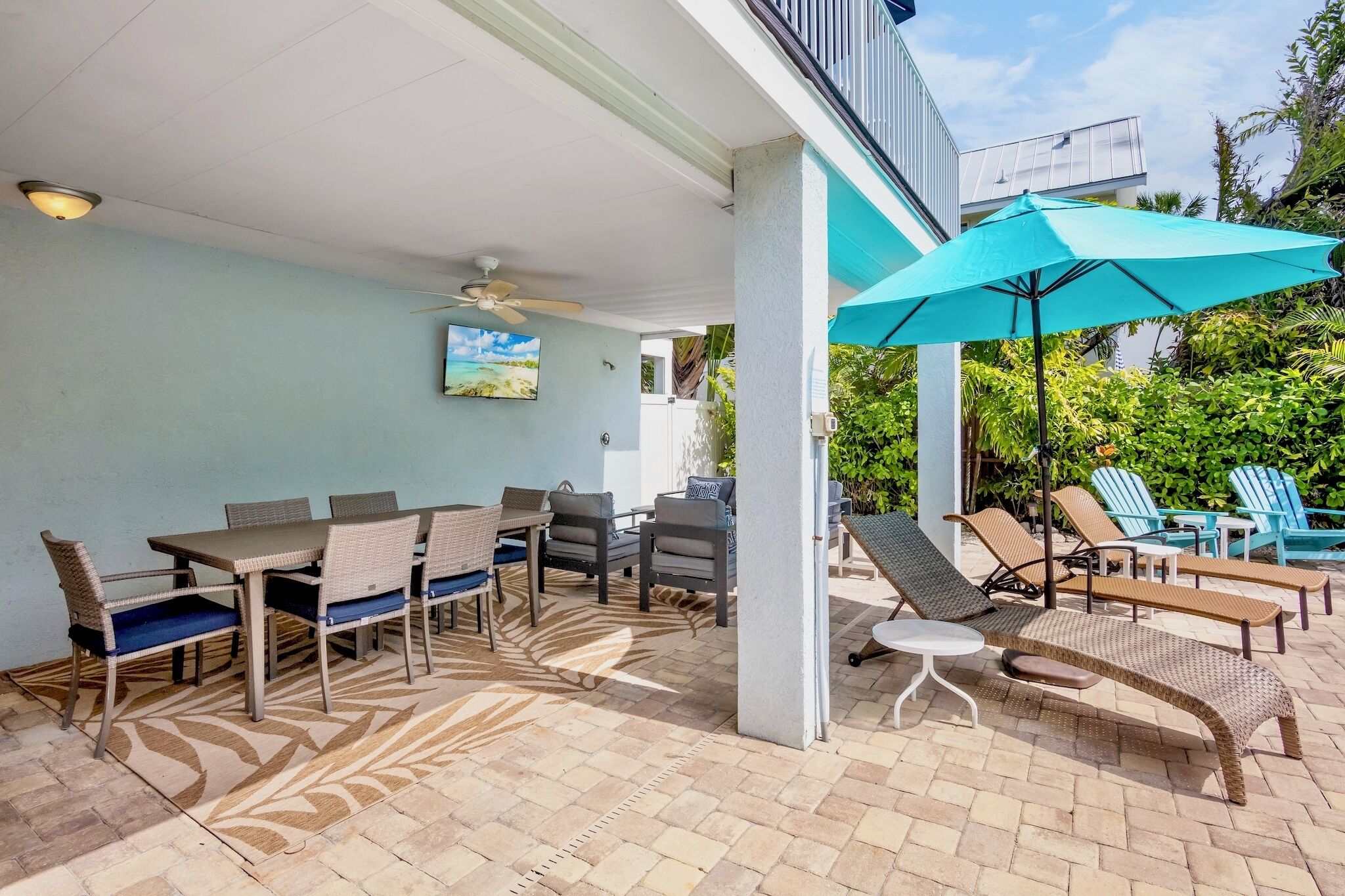 A covered patio area with a dining table and chairs, a lounge chair, and a ceiling fan.