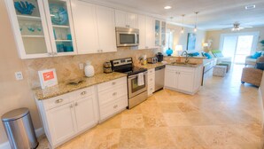A modern kitchen with white cabinetry, a granite countertop, stainless steel appliances, and a small island with a sink.