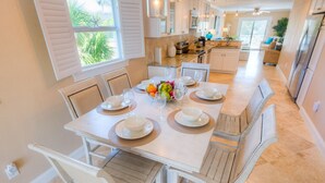 A dining area with a white table set for four, surrounded by white chairs with wooden accents.