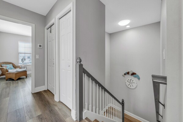 Un couloir avec un escalier, des portes blanches et un fauteuil en osier avec des coussins.