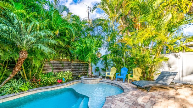 Una piscina rodeada de exuberante vegetación tropical, con un patio de piedra y sillas de descanso.