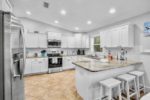 A modern kitchen with white cabinetry, stainless steel appliances, a granite countertop, and a built-in island with bar stools. - Pet Friendly Private Duplex. Fenced Yard with Private Pool Short Walk to Beach (Holmes Beach)