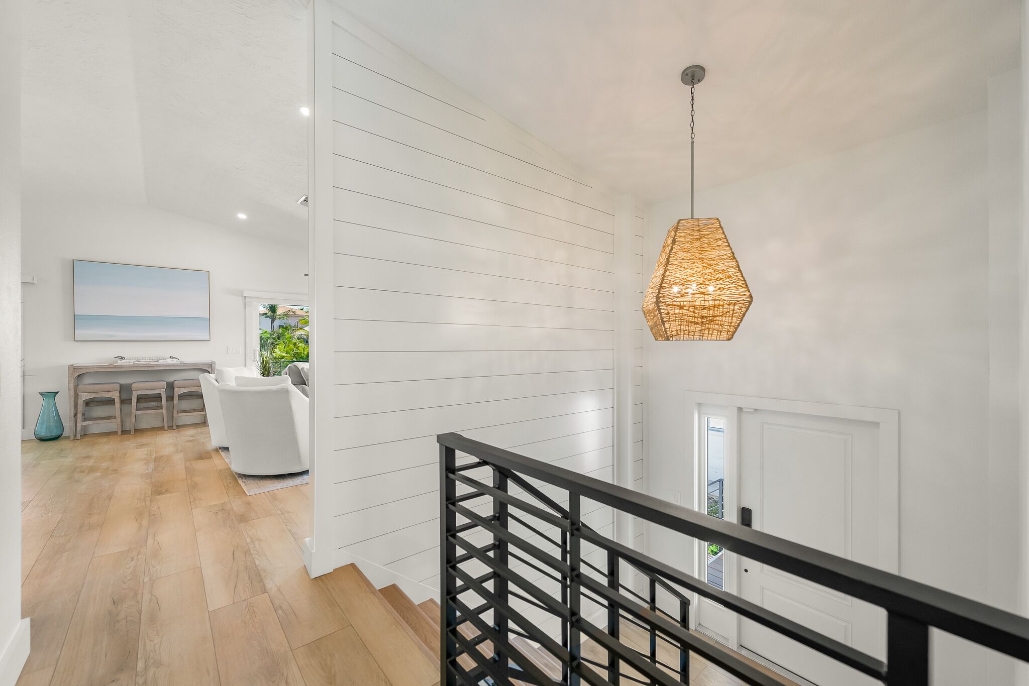 A modern interior with a staircase, a hanging light fixture, and a view of a kitchen area.