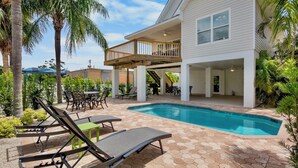 A backyard with a swimming pool, lounge chairs, a deck, and a covered patio area. - Large Private Beach Home! Heated Pool, Elevator, Balcony, and Near the Beach! (Holmes Beach)