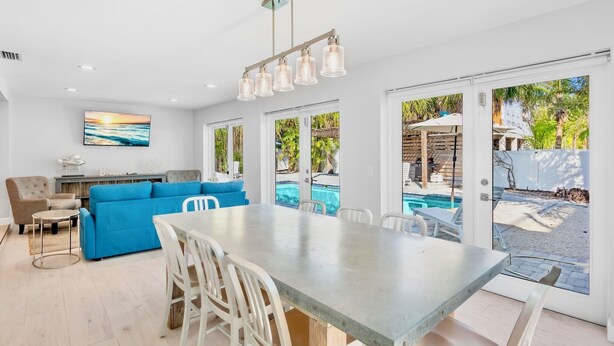 A spacious living area with a blue sofa, a dining table with chairs, and a view of a swimming pool through large sliding glass doors. - Private Duplex with Beautiful Updates and Heated Pool! 1 Minute from the Beach! (Anna Maria)