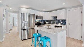 A modern kitchen with stainless steel appliances, a marble island, and blue bar stools. - Private Duplex with Beautiful Updates and Heated Pool! 1 Minute from the Beach! (Anna Maria)