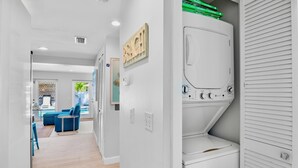 A laundry room with a white washer and dryer, a wooden sign, and a blue chair in the background. - Private Duplex with Beautiful Updates and Heated Pool! 1 Minute from the Beach! (Anna Maria)