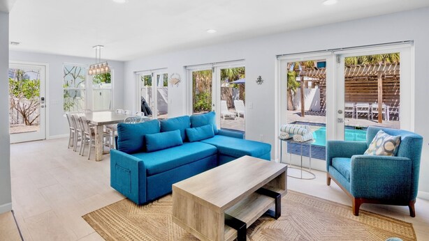 Un salon moderne avec un canapé d’angle bleu, une table basse en bois et une vue sur la piscine, visible à travers de grandes portes-fenêtres coulissantes.