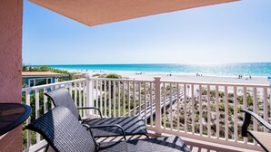 Un balcón con dos sillones de mimbre, una mesa y vista a la playa y al océano.