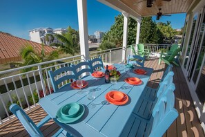 Uma área de refeições coberta ao ar livre, com uma mesa posta para quatro pessoas, rodeada por cadeiras azuis.