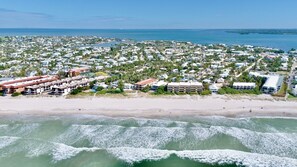 An aerial view of a coastal residential area with beachfront properties, a marina, and a bridge in the distance.