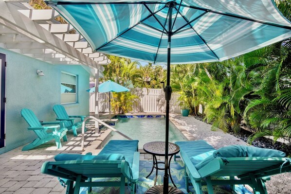 A pool area with lounge chairs, a small table, and a large umbrella.