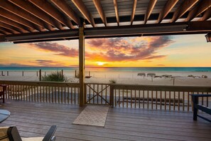 A wooden deck with a view of the beach and sunset.