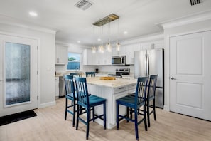 Une cuisine moderne avec des meubles blancs, un îlot central doté de chaises bleues, des appareils en acier inoxydable et des luminaires suspendus.