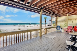 Une terrasse en bois offrant une vue sur la plage, avec des sièges d’extérieur et un palmier.