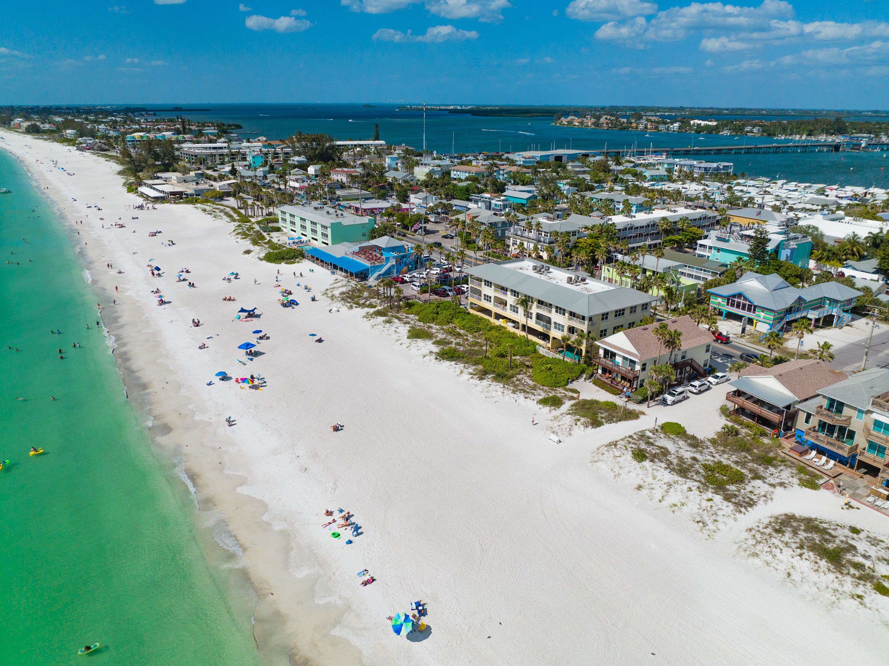 An aerial view of a beachside resort with multiple buildings, a sandy beach, and a marina.