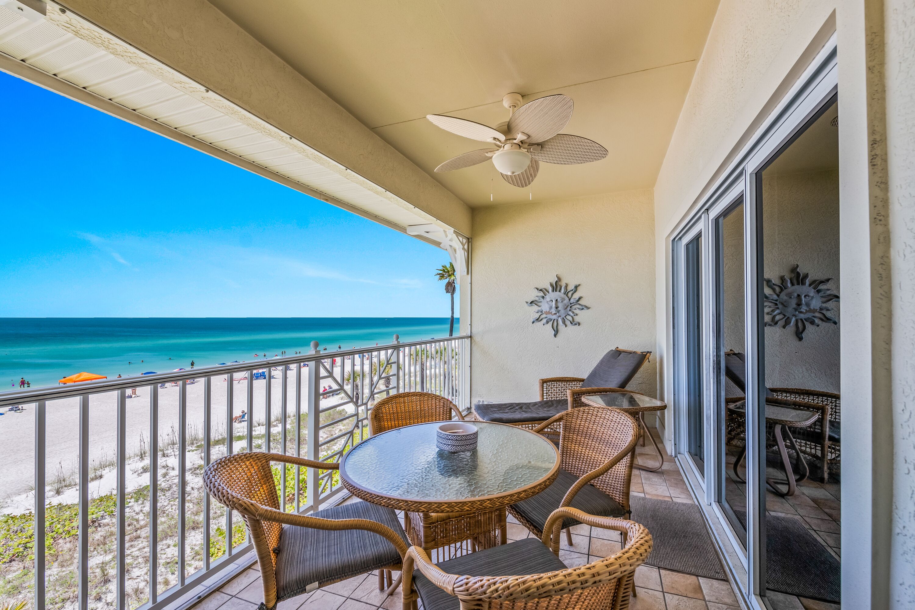 A balcony with wicker furniture, a ceiling fan, and a view of the beach.