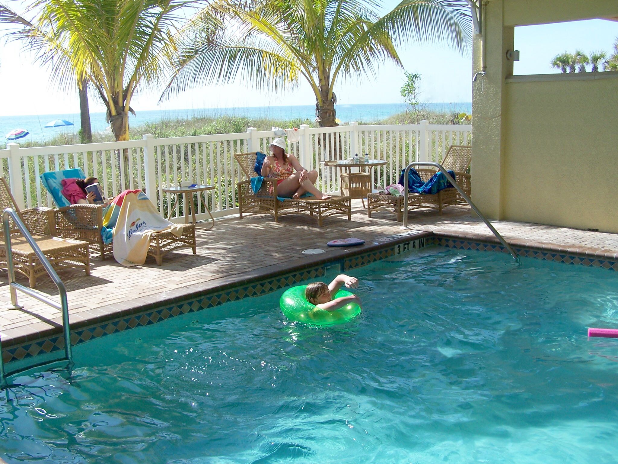 A pool area with lounge chairs, a small table, and a view of the ocean.