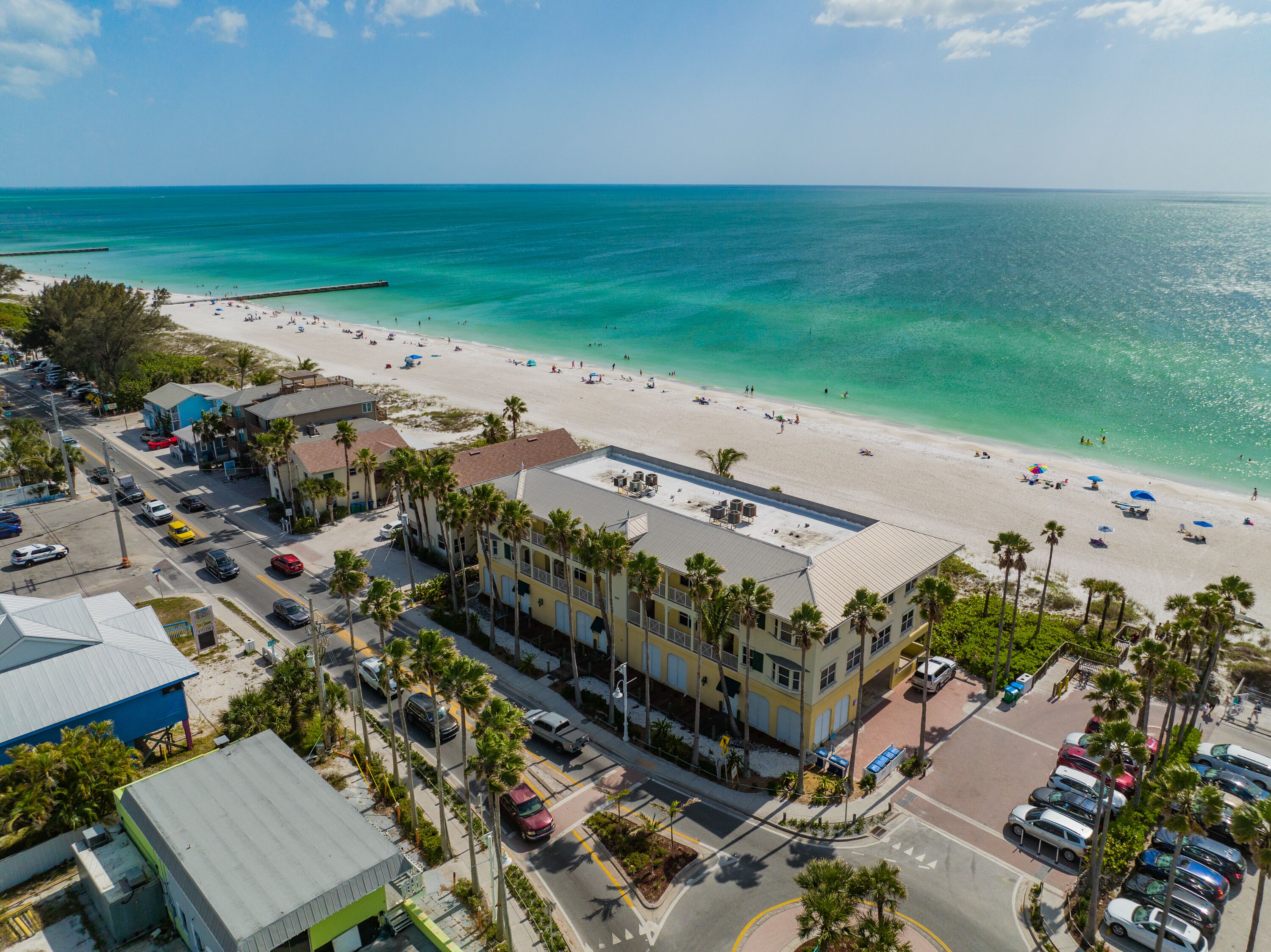 A coastal hotel with a beach view, multiple parking areas, and a street with cars.