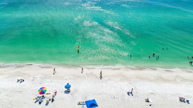 Ein Strand mit klarem türkisblauem Wasser, weißem Sand und Menschen, die schwimmen und sonnenbaden.