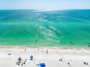 Een strand met helder turquoise water, wit zand en mensen die zwemmen en zonnebaden.