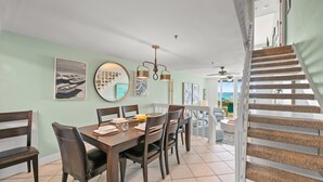 Un coin repas avec une table et des chaises en bois, un miroir rond et des œuvres d’art accrochées aux murs. Un escalier mène à un espace extérieur offrant une vue.