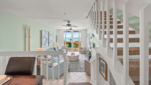 Un vaste espace de vie donnant sur l’extérieur, un coin repas avec une table et des chaises, et un escalier menant à un balcon.