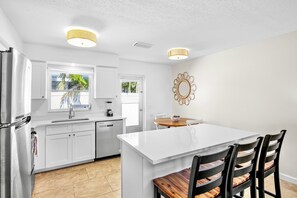 Enjoy meals and snacks at the central island with four chairs, surrounded by white cabinetry and a stainless steel refrigerator.