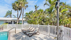 A poolside area with lounge chairs, a white fence, and palm trees.
