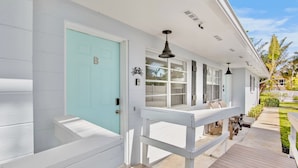 A coastal house with a light blue door, a covered porch with seating, and a view of the ocean.