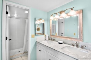 A bathroom with a shower, two sinks, a vanity, and a mirror with lights.