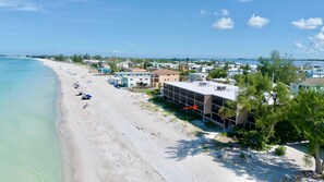 A beachside hotel with a sandy beach, clear blue water, and a view of the ocean.