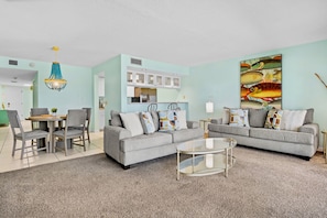 A living room with a grey sofa, a glass coffee table, and a dining area with chairs and a table.
