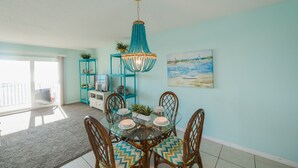 A dining area with a glass table, wooden chairs, a turquoise pendant light, and a painting on the wall.
