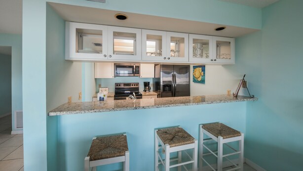 A kitchen with white cabinets, a microwave, a stove, and a refrigerator. There are two stools with woven seats.