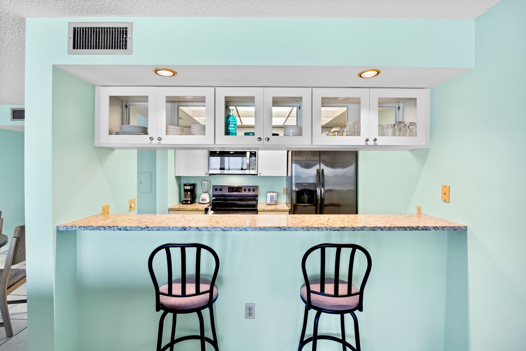 Una cocina compacta con una isla central, dos taburetes de bar y un refrigerador.