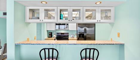 Una cocina compacta con una isla central, dos taburetes de bar y un refrigerador.