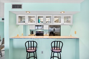 A compact kitchen with a central island, two bar stools, and a refrigerator. - Family-friendly Beachfront Condo with Pool! (Bradenton Beach)