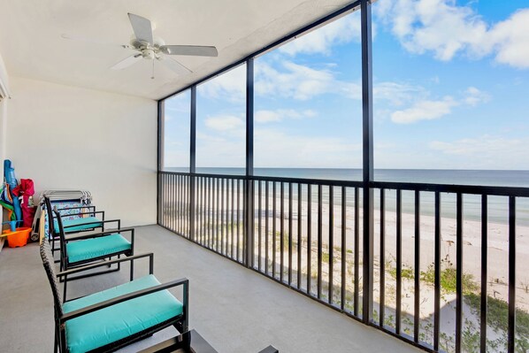 A balcony with a view of the beach, equipped with chairs and a ceiling fan.