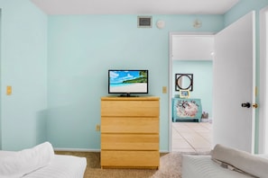 A room with a television on a wooden dresser, a door leading to another room, and a white wall.