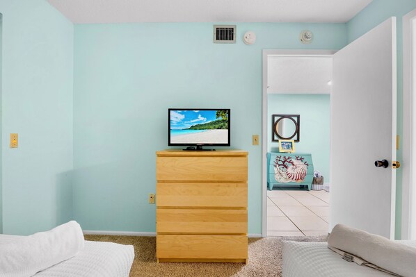 Una habitación con una televisión sobre un aparador de madera, una puerta que conduce a otra estancia y una pared blanca.