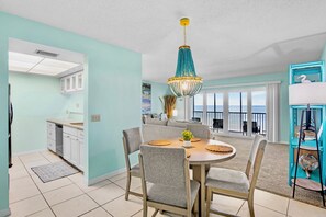 A modern kitchen with white cabinets, a dining area with a round table, and a balcony with a view.