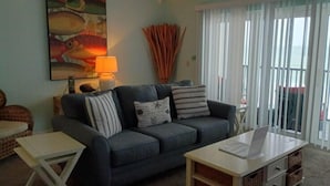 A living room with a dark blue sofa, a small white side table, a lamp, and a painting of fish on the wall.