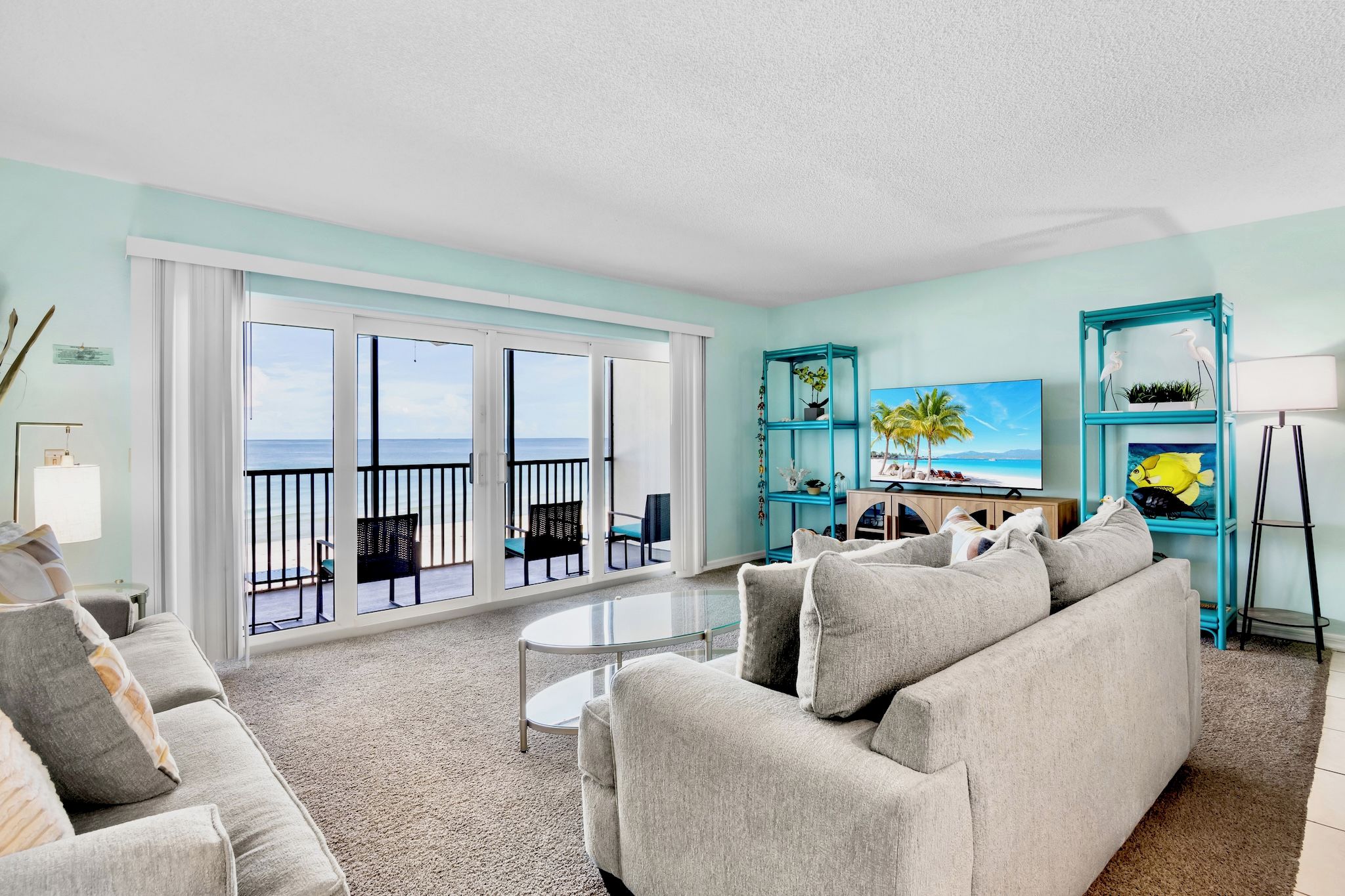 A living room with a view of the ocean, a sofa, a coffee table, and a TV on a stand.