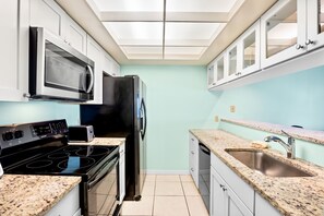 Una cocina compacta con microondas, estufa, refrigerador y lavamanos.