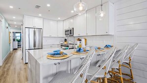 A modern kitchen with white cabinetry, a central island with seating, and a stainless steel refrigerator.