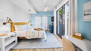 A bedroom with a bed, bedside table, lamp, and a view of the outdoors.